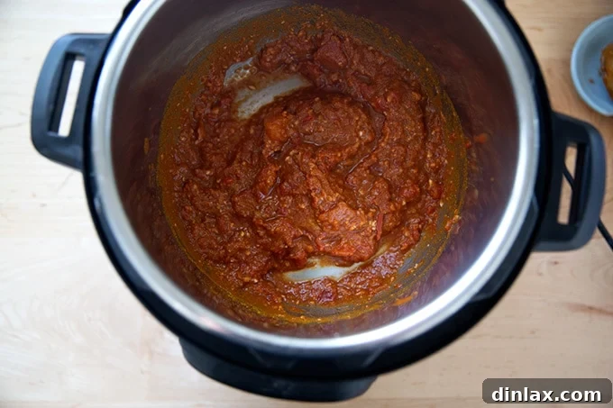Effortless Butter Chicken and Chickpeas Instant Pot or Stovetop 7 Close-up of an Instant Pot, showing the vibrant mixture of tomatoes, ginger, garlic, salt, and curry powder, stirred together.