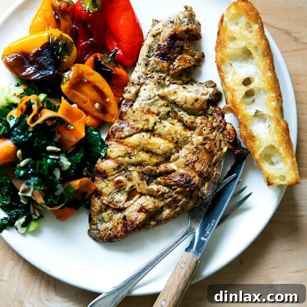 Grilled chicken breast on a plate aside bread, peppers, and salad.