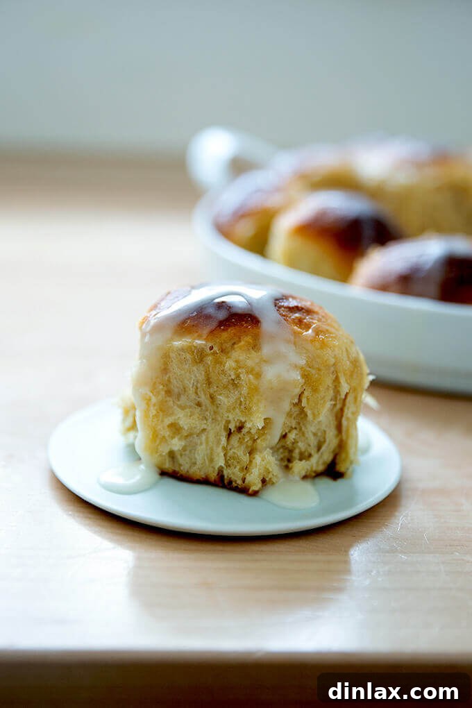 A close-up of a single hot cross bun, revealing its tender crumb and delicate glaze.