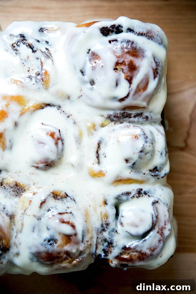 A pan of golden, swirled brioche cinnamon buns with a luscious cream cheese frosting.