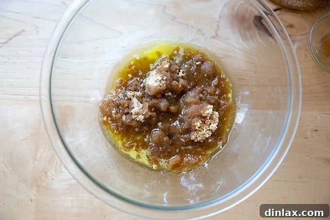 A glass bowl containing just-melted butter, rich brown sugar, and a splash of vanilla extract, ready to be whisked into the cookie dough base.