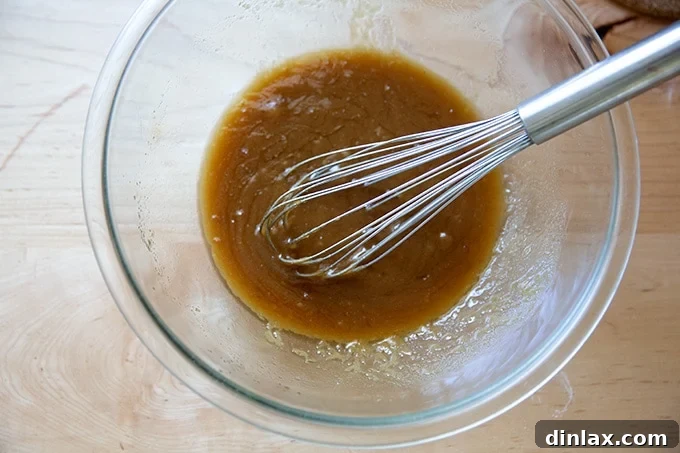 The melted butter, vanilla, and brown sugar mixture after being thoroughly whisked together, forming a smooth and glossy foundation for the peanut butter cookie dough.