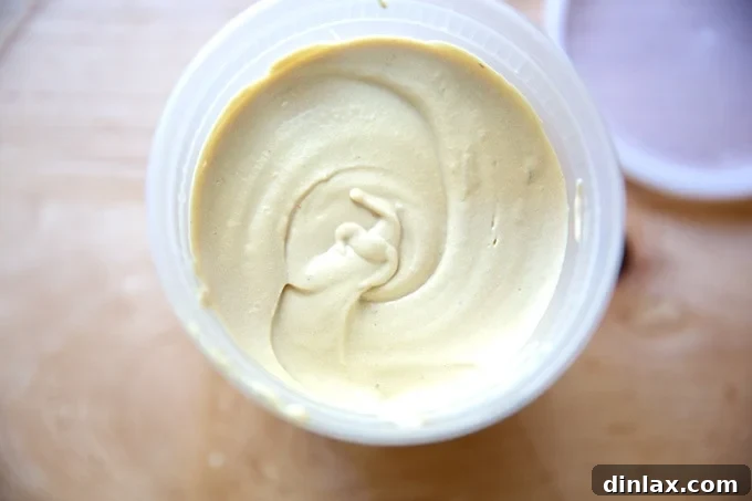 A quart-sized container filled with exceptionally creamy hummus, indicative of a batch made with a high-speed blender like a Vitamix.