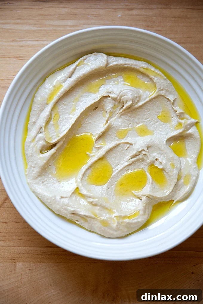 A platter of homemade hummus made in a food processor, appearing creamy with a slightly less silken texture compared to the Vitamix version, elegantly drizzled with olive oil.