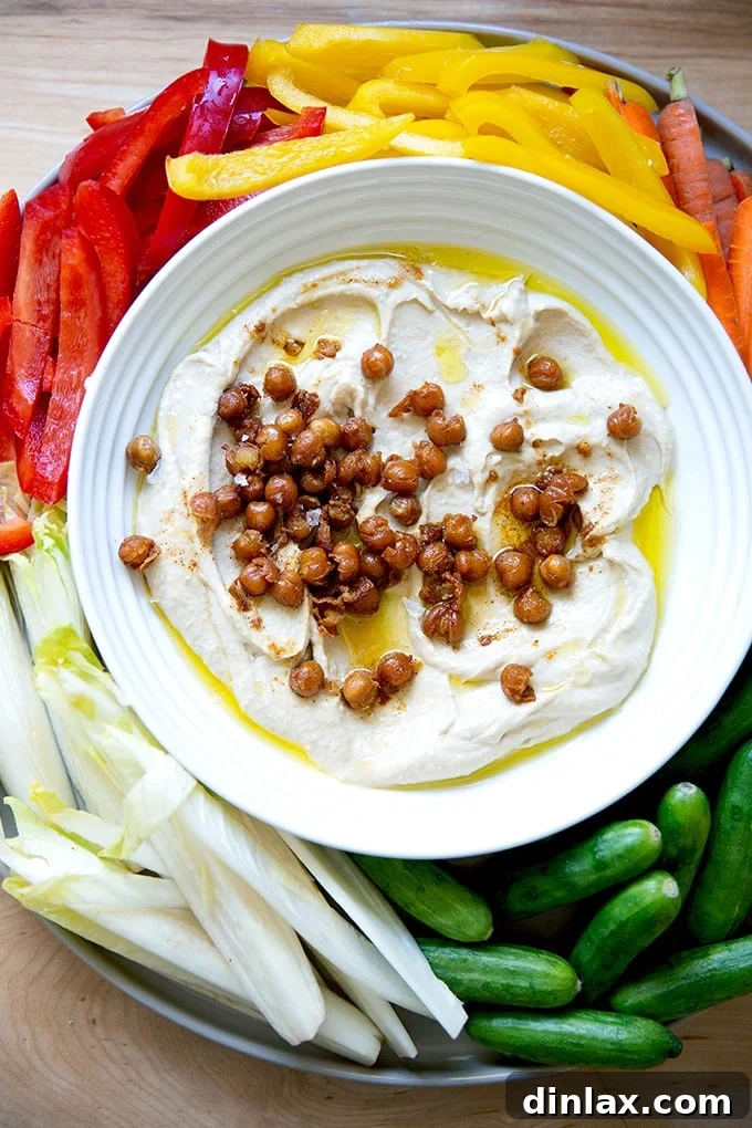 A vibrant platter showcasing homemade hummus surrounded by an array of fresh, colorful vegetables including sliced bell peppers, carrots, and cucumber sticks, inviting healthy snacking.