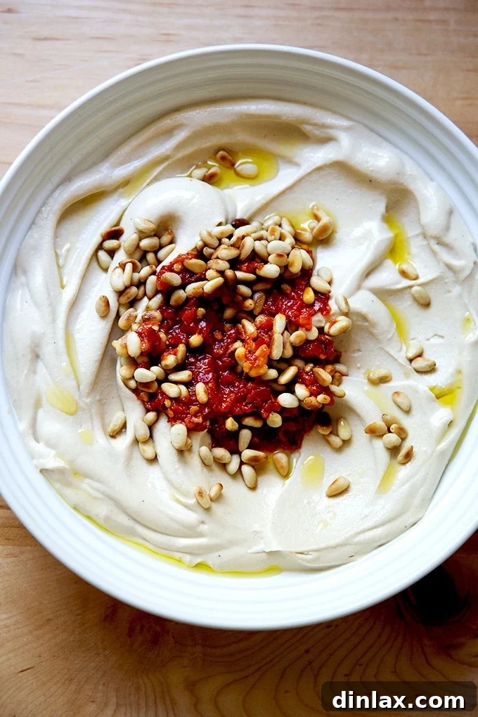 A bowl of creamy hummus garnished with a swirl of red chili paste and a sprinkle of toasted pine nuts, presenting an inviting and flavorful combination.