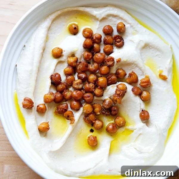 A platter of homemade hummus topped with crispy chickpeas, olive oil, and fresh herbs, surrounded by colorful vegetables, ready for serving.
