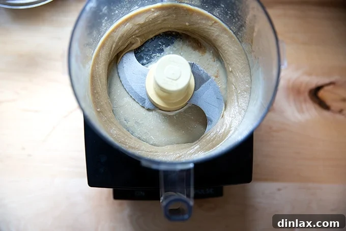 The tahini, salt, lemon, and cumin mixture in the food processor after initial blending, now resembling a thick, creamy peanut butter.