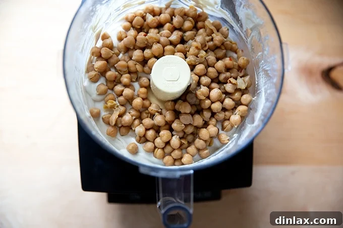A food processor bowl containing the hummus in progress, with chickpeas added to the tahini base, ready for the final blending stage.