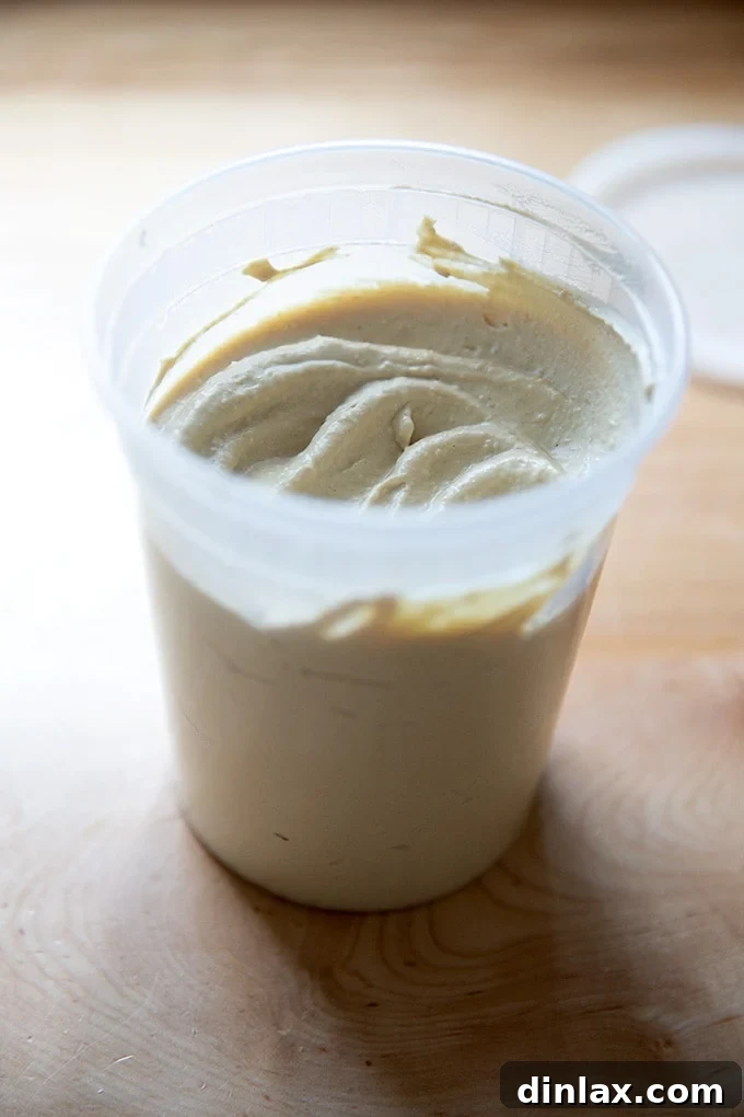 A clear glass tub filled with a generous portion of homemade hummus, showcasing its creamy texture, prepared and ready for refrigeration.