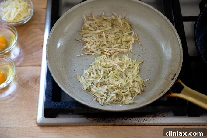 A nonstick skillet on medium heat, showcasing two thin piles of grated potato sizzling in olive oil, lightly seasoned.