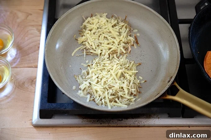 Two mounds of grated potato crisping in a skillet, topped with a generous sprinkle of melting grated cheese, forming golden edges.