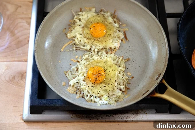 Two eggs, cracked over crispy potato and cheese in a skillet, seasoned with salt and pepper, cooking gently.