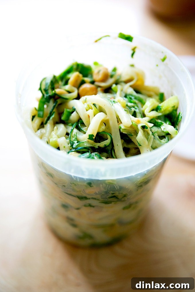 Refreshing Peanut Noodle Salad with Crisp Cucumbers 16 A quart container neatly filled with a portion of cold peanut noodles, topped with cucumbers and scallions, indicating its suitability for meal prep and storage.