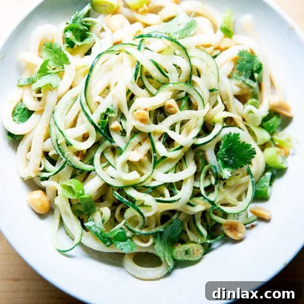 A bowl of cold peanut noodles with crisp cucumbers, fresh scallions, and crunchy peanuts, beautifully garnished for serving.