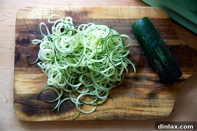 Refreshing Peanut Noodle Salad with Crisp Cucumbers 8 A pile of freshly spiralized cucumbers resting on a wooden cutting board, showcasing their delicate and curly texture.