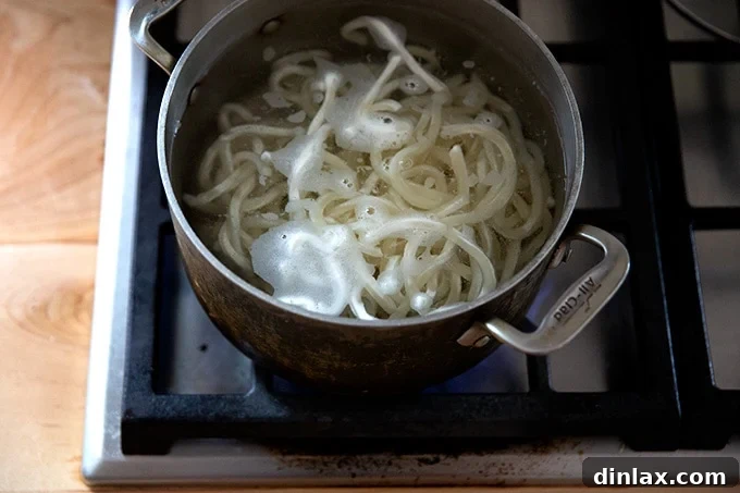 Refreshing Peanut Noodle Salad with Crisp Cucumbers 9 A pot of thick udon noodles boiling vigorously on a stovetop, capturing the steam and the bubbling water.