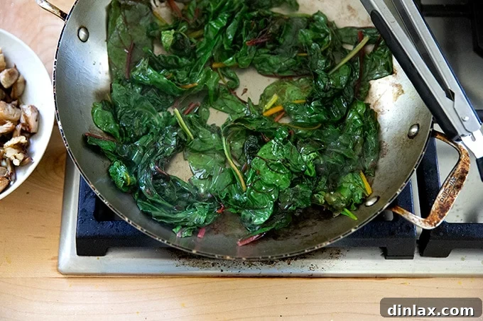 Effortless Butternut Squash Lasagna with Hearty Greens and Mushrooms 8 Tender, sautéed Swiss chard leaves glistening in a skillet, having wilted down perfectly for the lasagna.