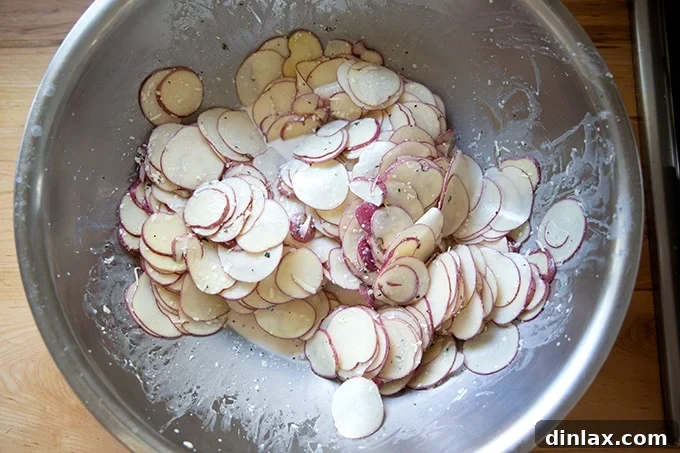An enormous mixing bowl brimming with thinly sliced potatoes coated in a creamy, herbaceous sauce.