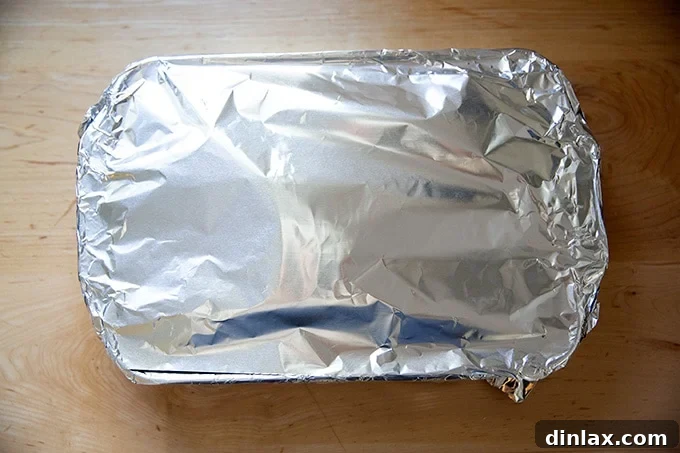 A 9x13-inch baking dish, tightly covered with aluminum foil, resting on a countertop.