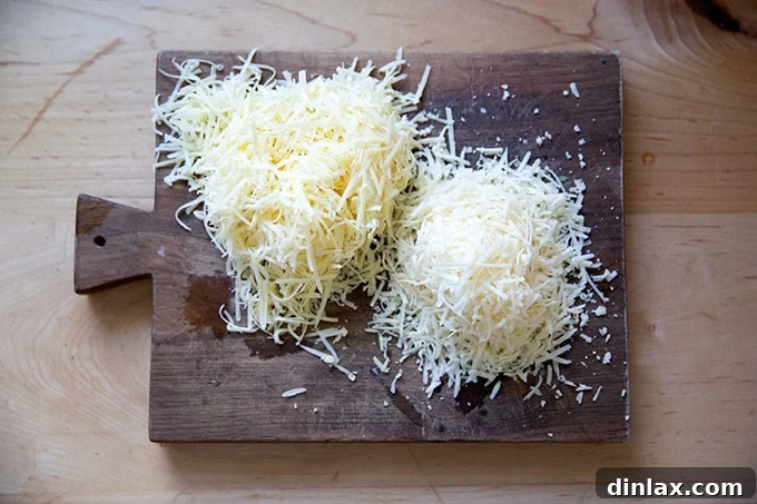 Two neat piles of freshly grated cheese – Gruyère and Parmesan – arranged on a wooden cutting board.