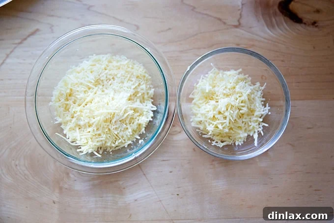 Two bowls of grated cheese on a countertop, with a smaller bowl containing the reserved portion.
