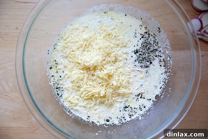 A large mixing bowl filled with a creamy liquid mixture, grated cheese, and green thyme sprigs.