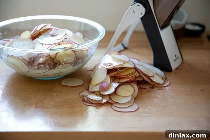 Finely sliced potatoes neatly arranged on a countertop beside a mandoline slicer.