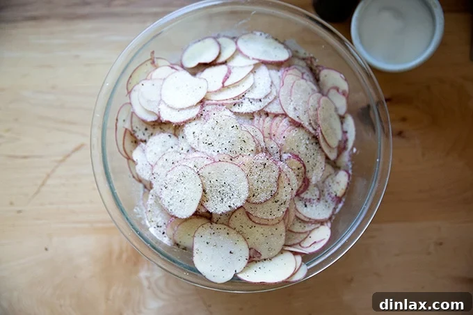 A large mixing bowl filled with thinly sliced potatoes, glistening with a creamy sauce.