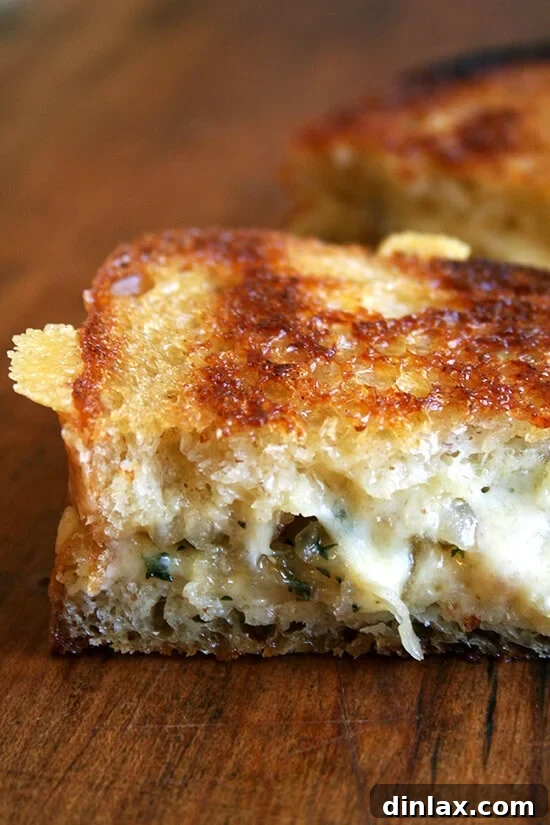A classic grilled cheese sandwich cut in half, revealing perfectly melted cheese and caramelized shallots between golden-brown country white bread slices.