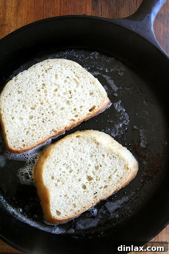Thick slices of artisan peasant bread toasting in a well-seasoned cast iron skillet, browning evenly.