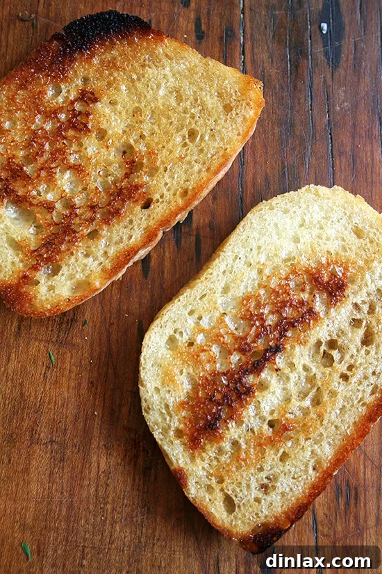 A close-up view of a half-finished grilled cheese sandwich, showing bread slices crisping in a skillet before cheese and shallots are added.