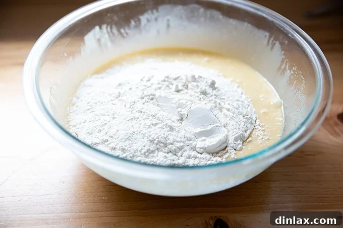 Flour has been added to the wet ingredients, and a spatula is poised to gently fold it in, completing the pound cake batter.