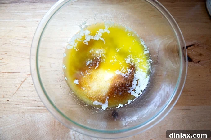 A close-up of a large mixing bowl, where melted butter, sugars, and salt are being whisked together, forming the base of the pound cake batter.