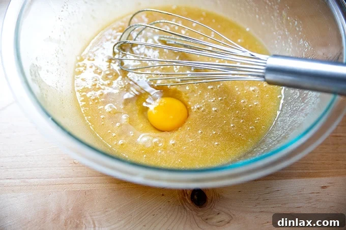 A hand cracks an egg into the large bowl containing the butter and sugar mixture, showing the step-by-step process of adding ingredients.