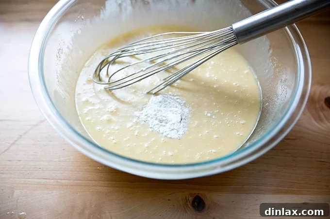 Baking powder being sprinkled over the wet ingredients in the bowl, ready to be whisked in for leavening.