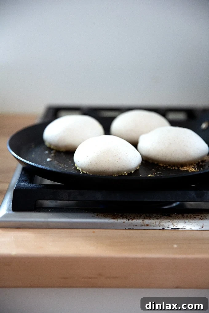 Browning sourdough English muffin dough balls in a skillet on the stovetop.