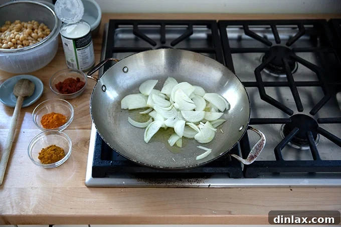 A large skillet on the stovetop, containing sliced onions glistening in olive oil as they begin to sauté and soften, releasing their sweet aroma.
