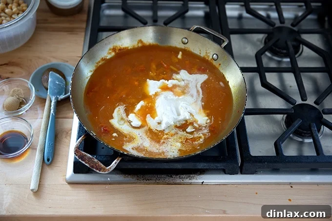The skillet on the stovetop with the curry base, now infused with coconut milk and water, being gently stirred to combine for a rich and creamy sauce.