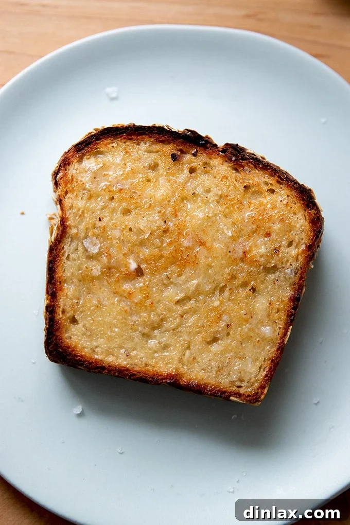 A perfectly toasted slice of no-knead maple oat bread on a white plate, ready to be enjoyed.