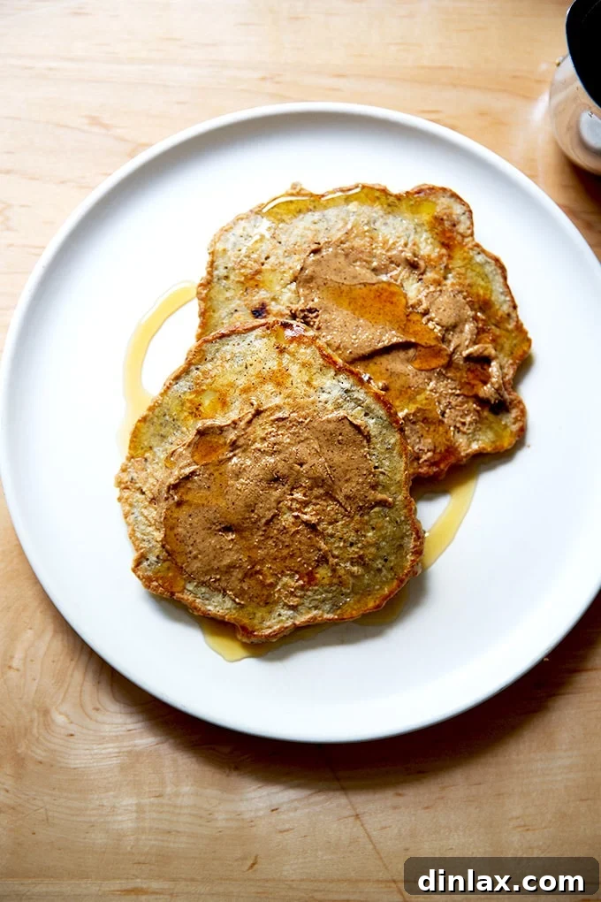 Banana-oat pancakes on a plate with almond butter and maple syrup.