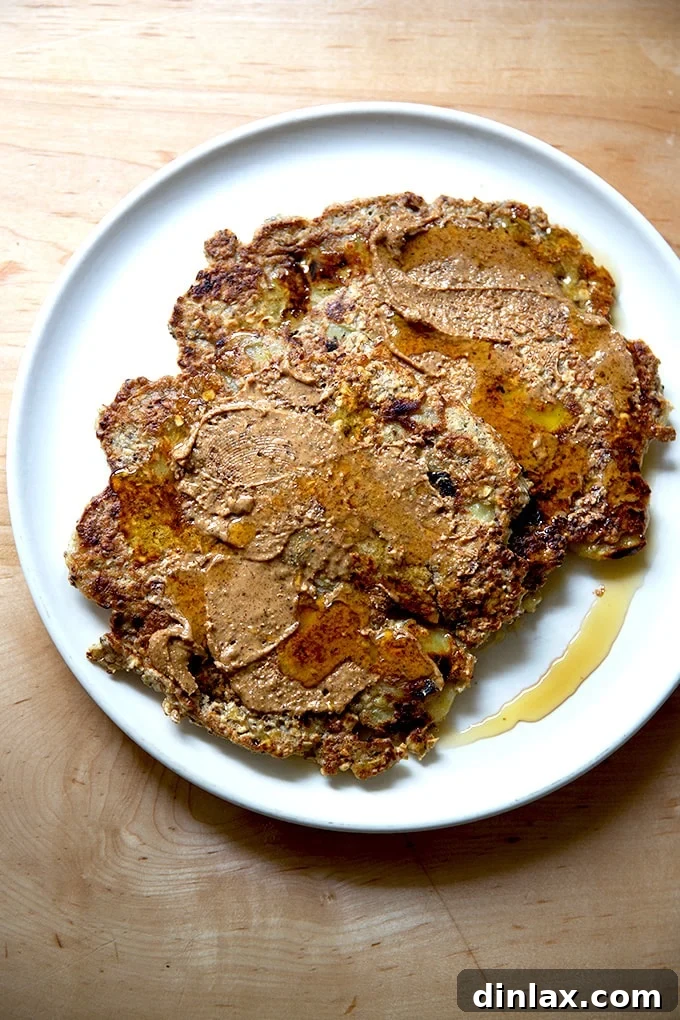 Banana-oat pancakes on a plate with almond butter and maple syrup.