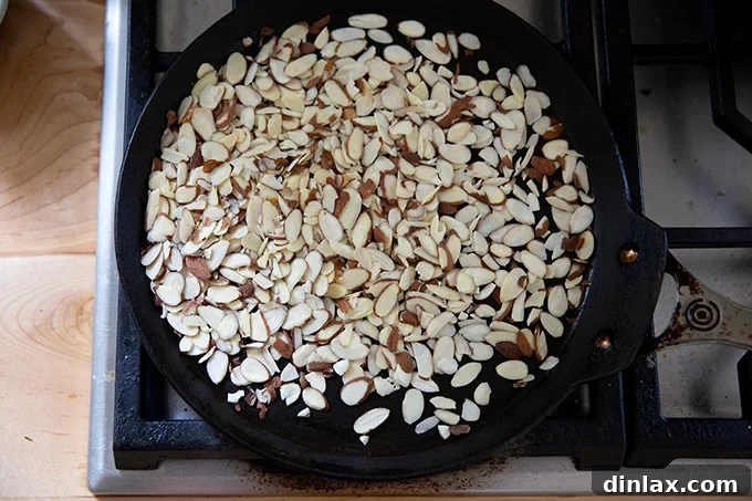 Sliced almonds toasting slowly in a skillet on the stovetop.