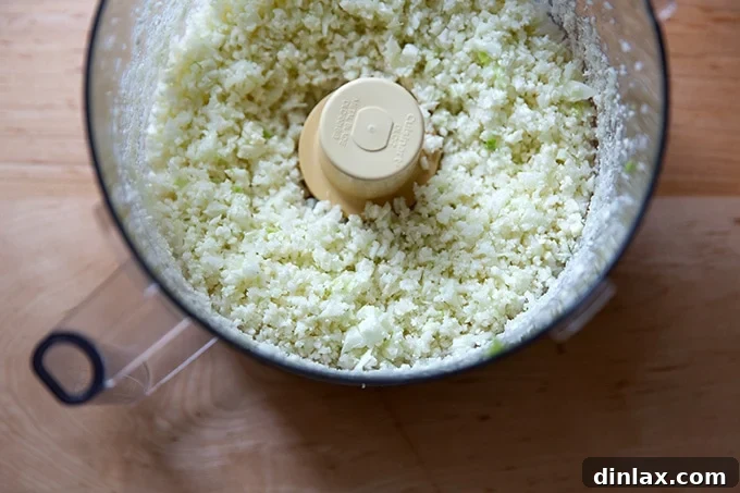 Finely chopped cauliflower resembling couscous in a food processor bowl.