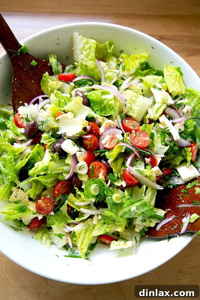 A vibrant, tossed Greek salad in a large white bowl, glistening with homemade dressing.