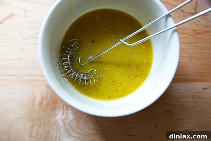 A bowl of perfectly whisked Greek salad dressing with a whisk resting inside, showcasing its emulsified texture.