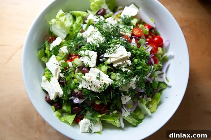 A large white bowl filled with untossed Greek salad ingredients, waiting for dressing.