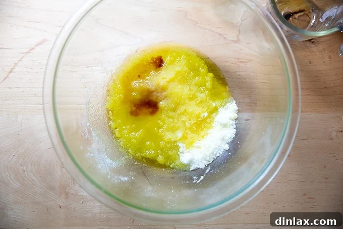 Effortless Lemon Blueberry Bread 6 A bowl with lemon-infused sugar, oil, and vanilla extract being whisked together, creating a pale yellow liquid mixture.