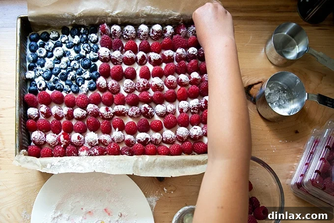 Effortless Star-Spangled Sheet Cake 14 A close-up of hands meticulously arranging blueberries and raspberries on the frosted cake to create the American flag design.