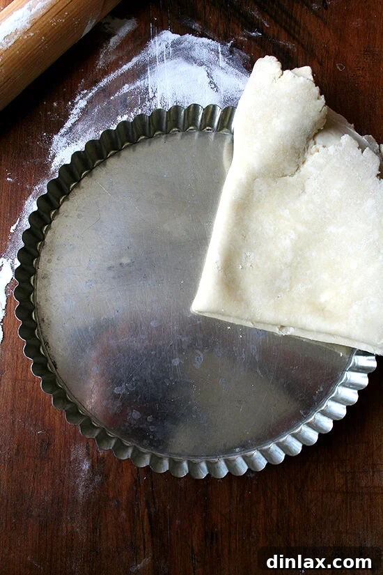 Carefully laying the dough into the tart pan, forming the perfect foundation. Rolling out and gently laying tart dough into a tart pan with a removable bottom, ensuring an even crust for the French apple tart.